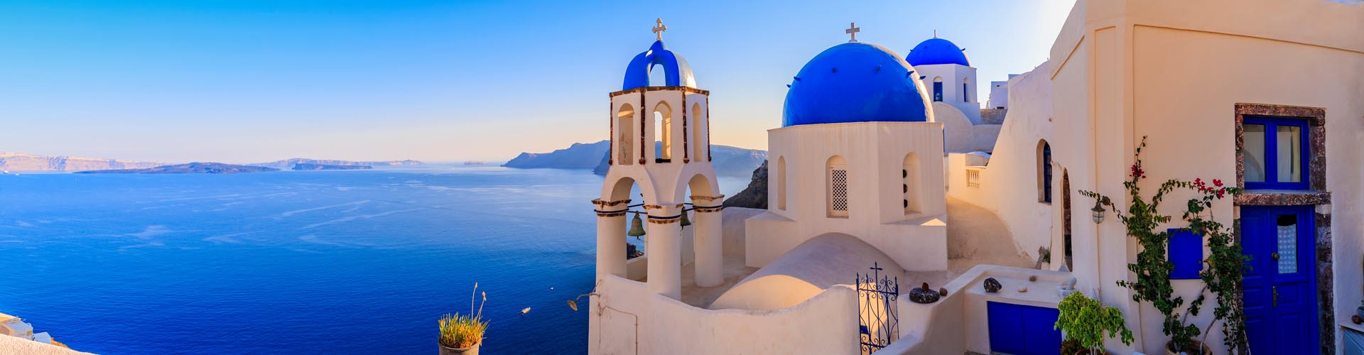 Türkisblaues Meer, weiße Häuser mit blauen Kuppeln - Urlaub in Griechenland, gut versichert mit Allianz Travel Reiseversicherungen!